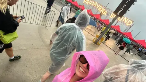 Lauren Cashell Lauren Cashell wears a pink rain poncho and sunglasses. Behind her is a bright sign that says 'Primavera Sound'.