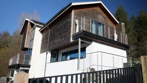 A two-storey building with white rendering on the bottom and wooden rendering on the top