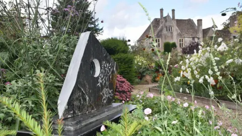 National Trust A stone sculpture with a hole in the middle and floral style carvings with Avebury manor in the background