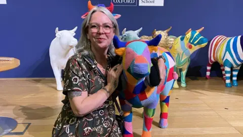 Sobell House Hospice Yarnsy the artist in ox horns sat next to her multi-coloured yarn ox sculpture called Tony