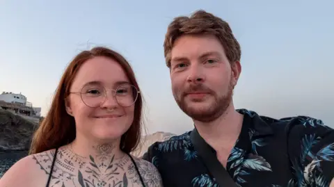 Stephen Whyte A selfie of Lauren Evans and Stephen Whyte. Lauren has red hair, glasses and tattoos on her chest and neck. Stephen has light hair with a beard and is wearing a dark top. 