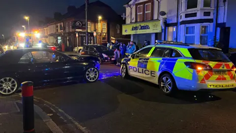 BBC/Shari Vahl A view of the crashed vehicles from behind, people are fathered to look on the street