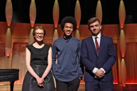 Jess Gillam (wearing black glasses and a black dress), Sheku Kanneh-Mason (wearing a dark blue shirt and black trousers) and Ben Goldscheider (in a navy suit with white shirt and dark red tie).
