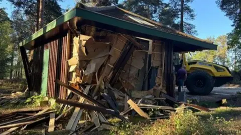 Forestry England A closer look at the damaged building. There is a partial hole in the side and splintered planks of wood are scattered around.