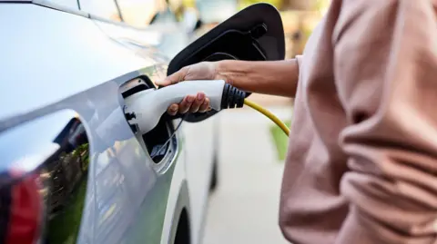 A woman plugs a charging cable into a grey electric car.