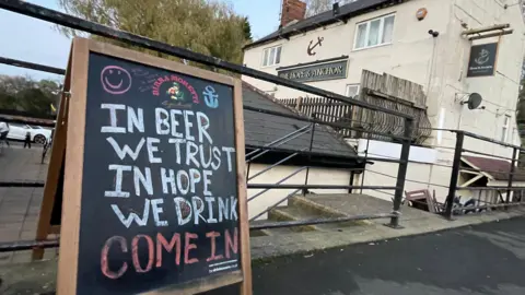 A pub blackboard outside the venue saying 'In beer we trust in hope we drink. Come in."