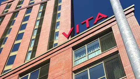 A red brick block building with a sign on top in read spelling out 'VITA' 