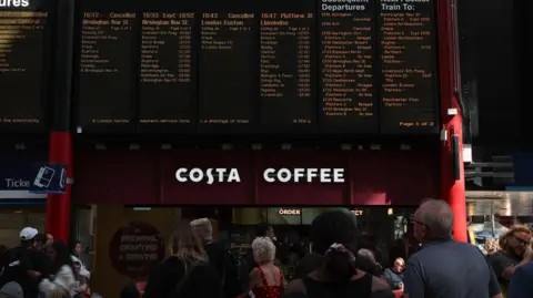 EPA/Shutterstock Passengers stand looking at departure boards at Liverpool Lime Street railway station as disruption continues
