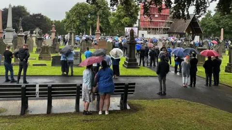 People watch the service streamed on a large screen outside the small chapel