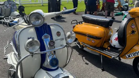 a white scooter with a blue stripe down the front next to an orange scooter