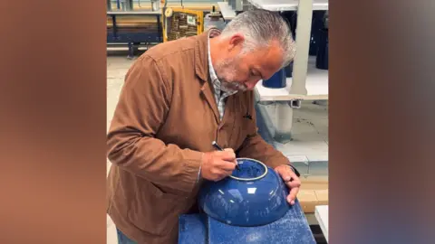 A man in brown jacket signing a blue bowl