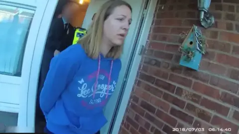 Cheshire Police Lucy Letby, with long straight hair and a blue hoodie, is led from her front door in handcuffs