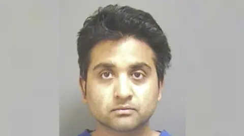A mugshot of a man looking toward the camera. He has dark hair and eyes.