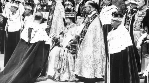 PA Media A black and white image from the coronation showing the Queen sitting on throne surrounded by clergy.