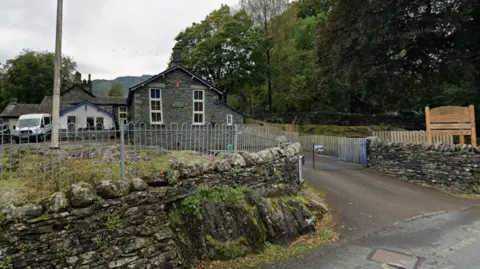 Langdale CofE Primary School in the Lake District, Cumbria. The school building is built with picturesque blue slate. It is in a green environment and has a dry stone wall surrounding the premises. 