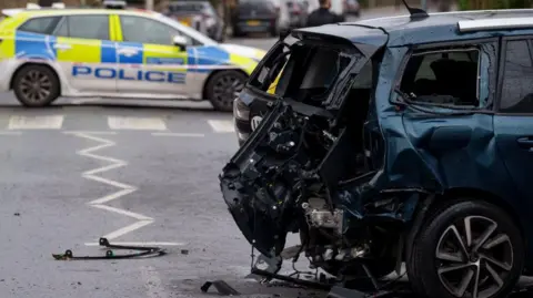 Getty Images The back of a car following a crash. In the distance a police car is parked behind police tape