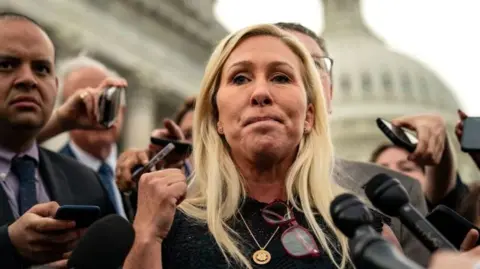 Marjorie Taylor Green speaks, as reporters shove microphones into her face