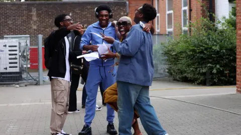 EPA/Shutterstock Three young men and a woman smiling as they celebrate A-level Results Day.