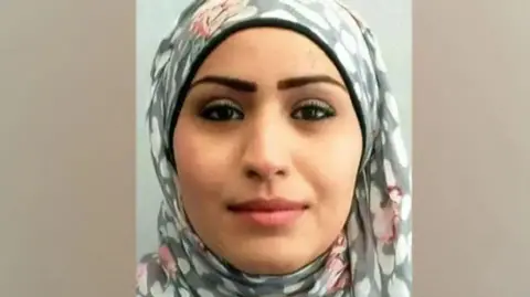 Rania Alayed wearing a grey, pink and white hijab with mascara on and lipstick looks impassively 