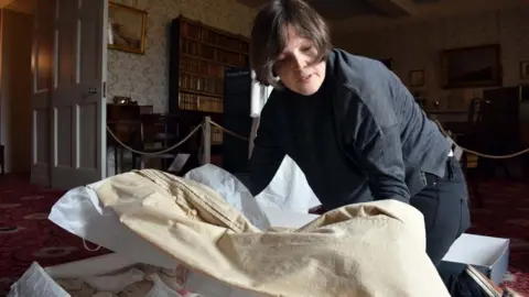 LCC Lynda Jackson, museum manager, examines a walking dress for display from around 1825