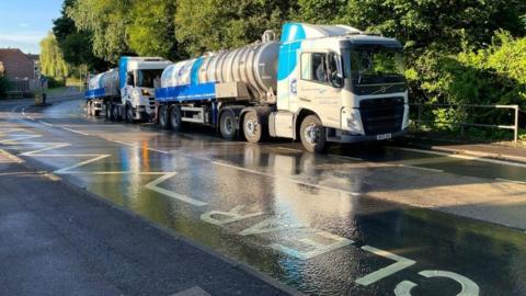 Two Southern Water tankers parked on a road with water seen running on yellow school road markings