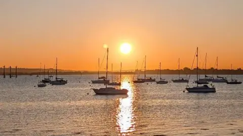 Sunrise Catcher Chloe Small boats on the water as an orange sun rises above the horizon