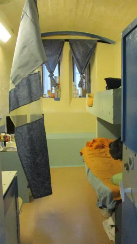 HM Inspectorate of Prisons Prison cell at HMP Leeds with blue curtains and door and an orange duvet cover.