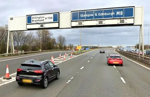 A Google view of the M8 motorway at Junction 26 shows the affected slip road. The gantry above the road bears the number 26 ans signposting for Hillington, Braehead, Glasgow and Edinburgh.