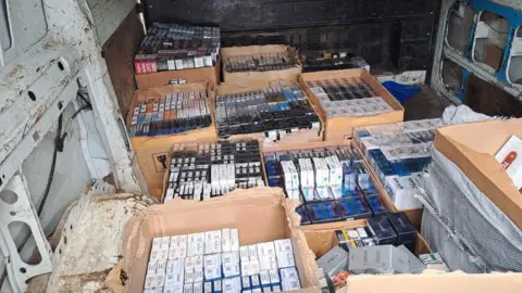 West Midlands Police Several brown cardboard boxes, seen in the back of a van, are filled with vapes and vaping products.