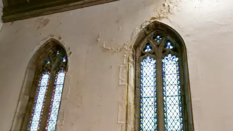 Diocese of Durham Crumbling paint surround the blue and red stained glass windows of the church .