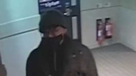 Northumbria Police Grainy CCTV of a antheral   wearing a achromatic  look   disguise  and hat.