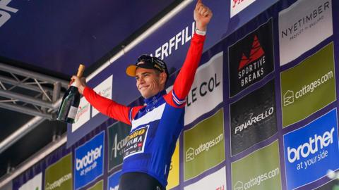 Wout van Aert holds his arms up on the winners' podium of the Tour of Britain