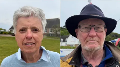 BBC Olive Thomas on the left is pictured in a blue jumper. Andrew Le Quesne is pictured in a yellow jacket and a black hat. He wears glasses. 
