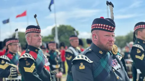 Members of the band looking ahead during the ceremony while flags fly in the background.