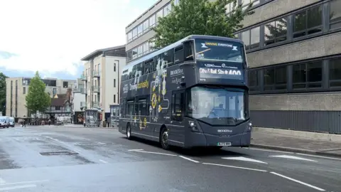A dark grey bus is seen on a road near the Westgate Shopping Centre in Oxford.