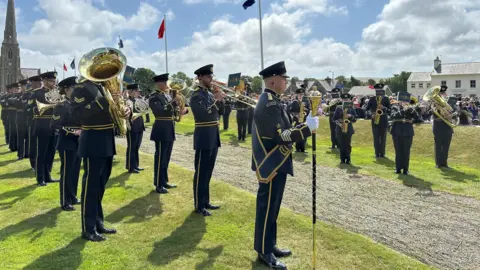 Band of the Royal Air Force College lining up either side of the ceremonial walkway. They are wearing grey uniforms with gold trim and are holding brass instruments.