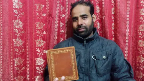 Ateeq Ahmad Man holding a book in front of a red cloth