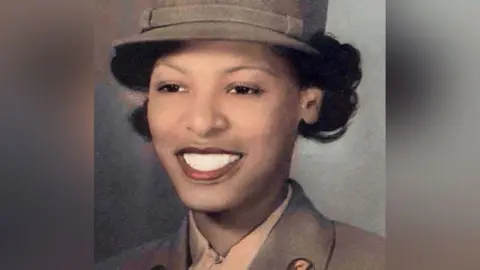 Evelyn Johnson who has short black hair underneath a brown US Women's Army Corps (WAC) cap. She is wearing a brown WAC uniform jacket, beneath which is a white shirt