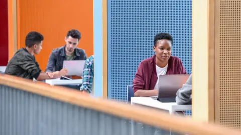 Students sitting at tables with laptops on a mezzanine balcony on a university campus in the UK