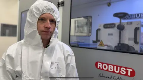 Richard LeCain pictured in a white hooded PPE protective jumpsuit. 