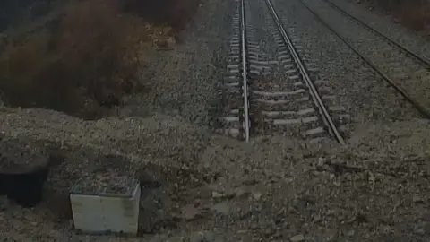 Network Rail Railway track covered in mud and stones, with trail of mud coming down the bank