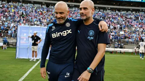 An image of Enzo Maresca, manager of Chelsea, and Pep Guardiola, manager of Man City embracing on the pitch.