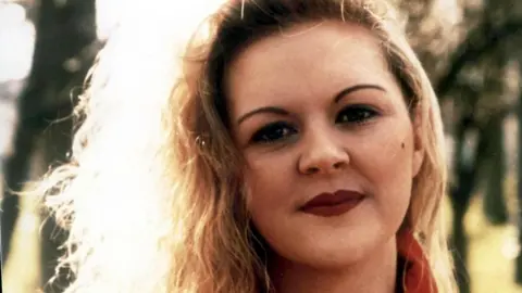Close shot of a woman with blonde curly hair, she is wearing red lipstick and a red top