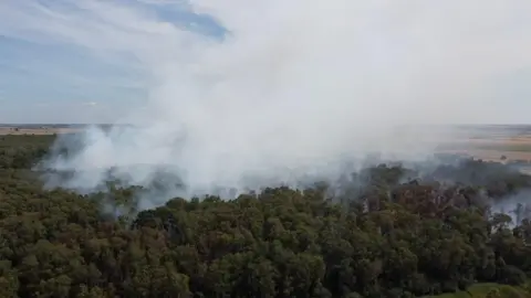 A drone image of the burning peatland, with plumes of white smoke in the air.