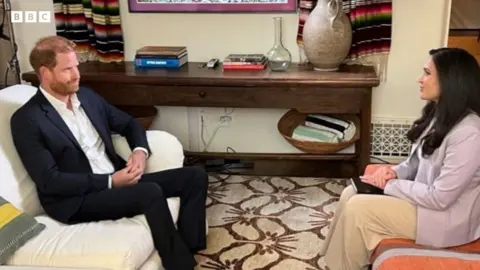 Duke of Sussex sat in a suit sat on a sofa opposite Nada Tawfik