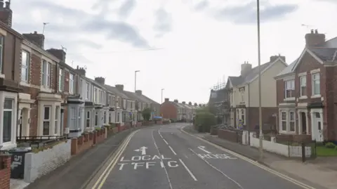 Two rows of terrace houses line Kent Street in Jarrow. They are made of red brick and have bay windows. 
