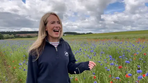 A woman with long blonde hair and a blue jumper stood in a confetti field with blue and red blooms