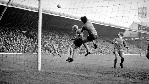 Getty Images Black and white of Parkes and Parking Jumping to intercept a ball in front of the goal posts. In the background is a big crowd at Anfield