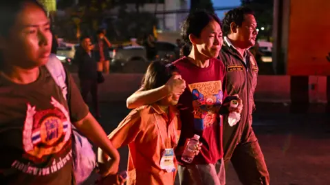 Getty Images Een familielid van een student die omkwam bij een busbrand bedekt de ogen van een jong familielid terwijl hij langs het wrak van de bus loopt 