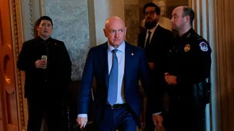 US Senator Mark Kelly seen walking through the halls of Congress, flanked by police and staff